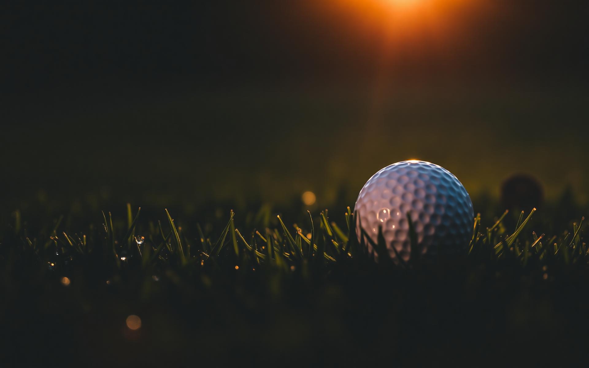Golf ball glowing in dew-covered fairway grass at sunrise